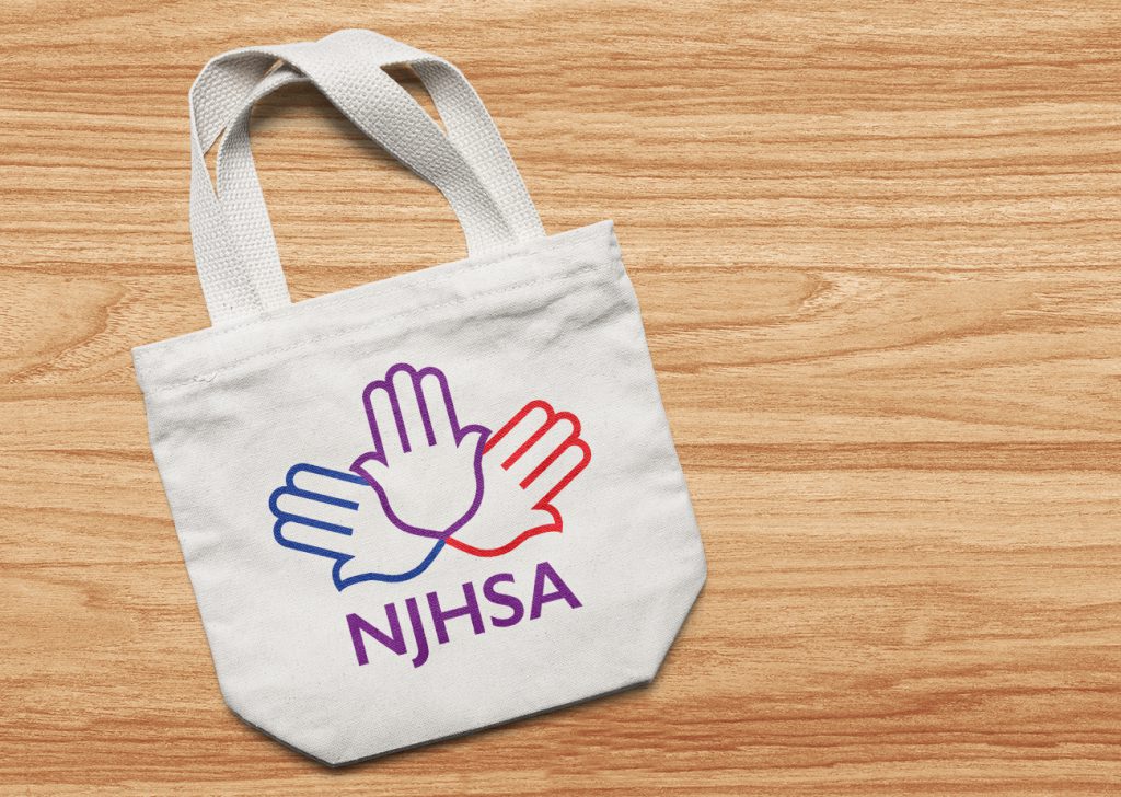 NJHSA Logo Bag | Logo is 3 Hamsa symbols arranged in a fan joined at the base of the palm. Colors are blue, purple and red with the letters NJHSA in purple capital sans-serif letters beneath. Logo is superimposed on off-white canvas tote bag.