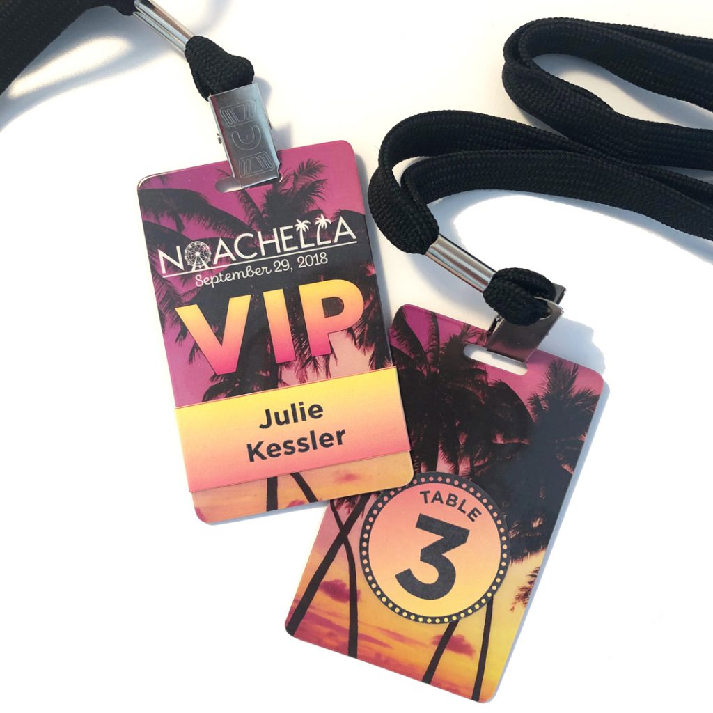 Plastic VIP pass cards, printed with logo and palm tree photo, guest's name on one side and table number on the other, hung from black lanyard with silver metal clip.