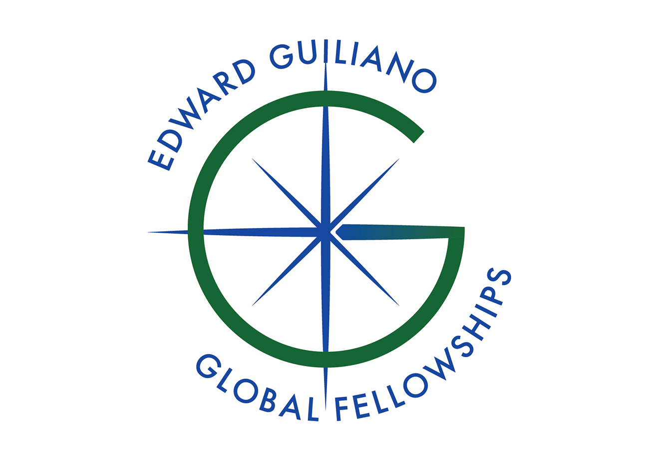 Logo for the Edward Guiliano Global Fellowships program. Symbol looks like a blue compass surrounded by a green capital letter G. The compass has sharp-looking crossed lines pointing north, south, west, and east, and shorter sharp points at a diagonal for northeast, northwest, southeast, and southwest. The eastern compass point also acts as the crossbar for the letter G, and a blue to green gradient transitions between the letter and the compass. The words "Edward Guilano" surround the arc at the top of the letter G in an all-capital letter serif font. This same font is used in the bottom of the G in another arc that says "Global Fellowships."