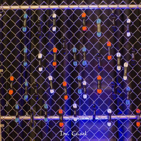 Bundles of white, blue, orange, and black shoelaces, wrapped with guests' names and table numbers, hanging from a chain-link fence.