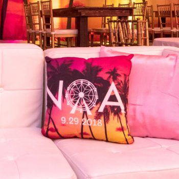 White lounge sofa with square throw pillow with logo and palm tree photo printed on it.