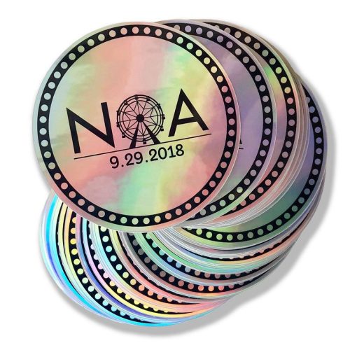 Stack of circular, holographic logo stickers with Noa logo imprinted in black.
